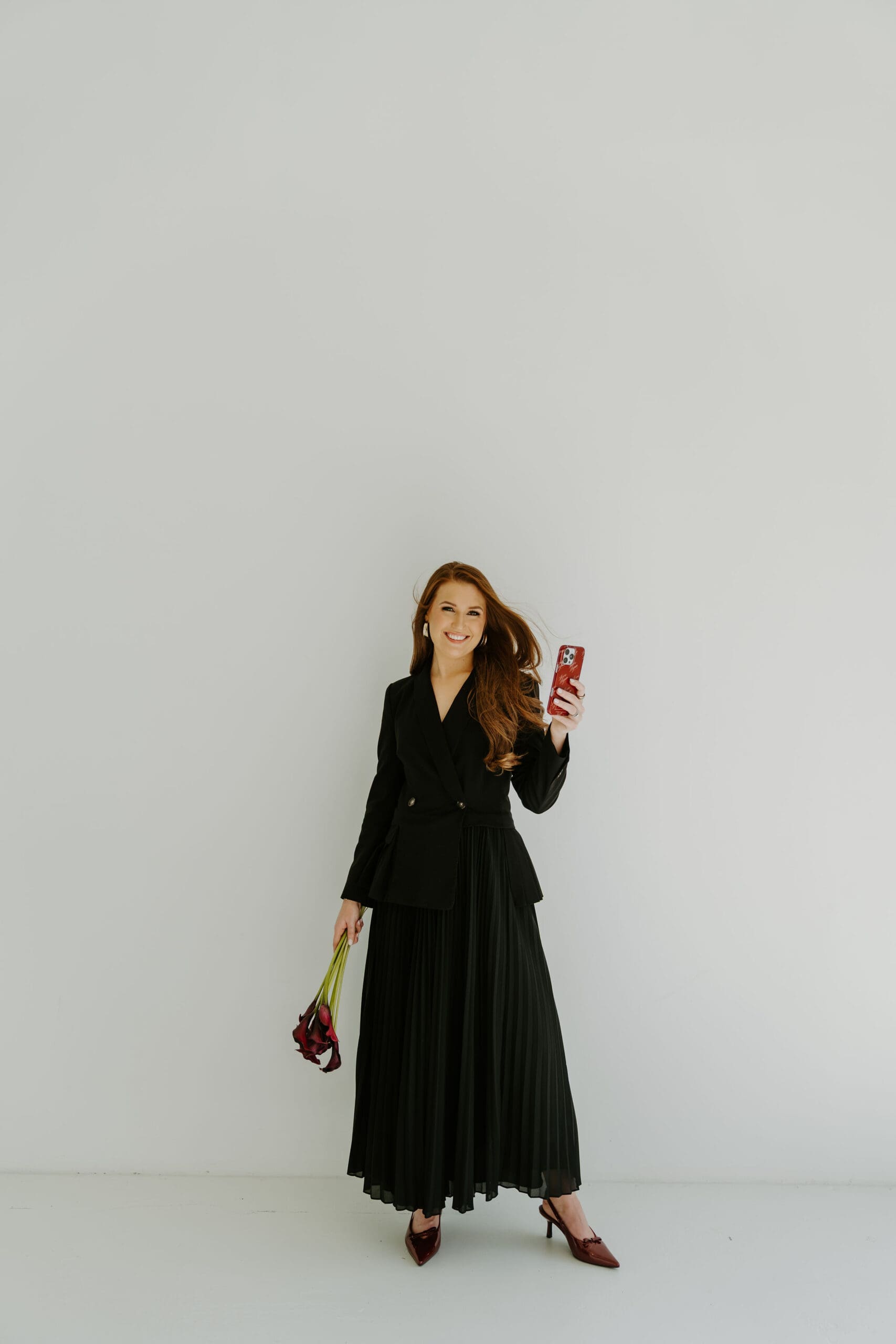 Logan, owner of Love by Logan, posing in a black blazer dress while holding an iPhone for a wedding content creator brand photoshoot in Atlanta Georgia